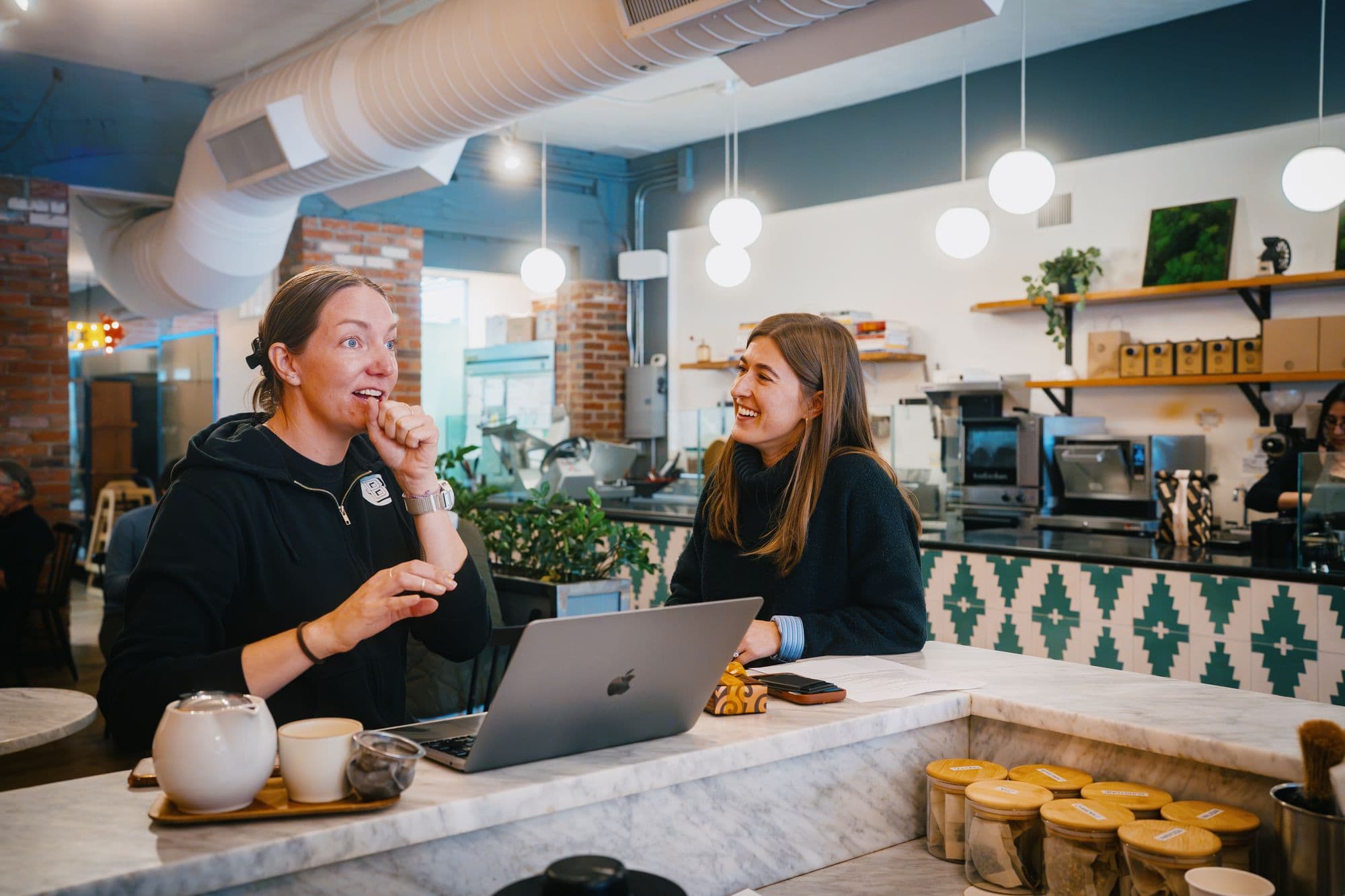 Linnea of Boxcar Coffee Roasters and Willow concierge Morgan Trego laughing at the marble counter inside Boxcar in Boulder