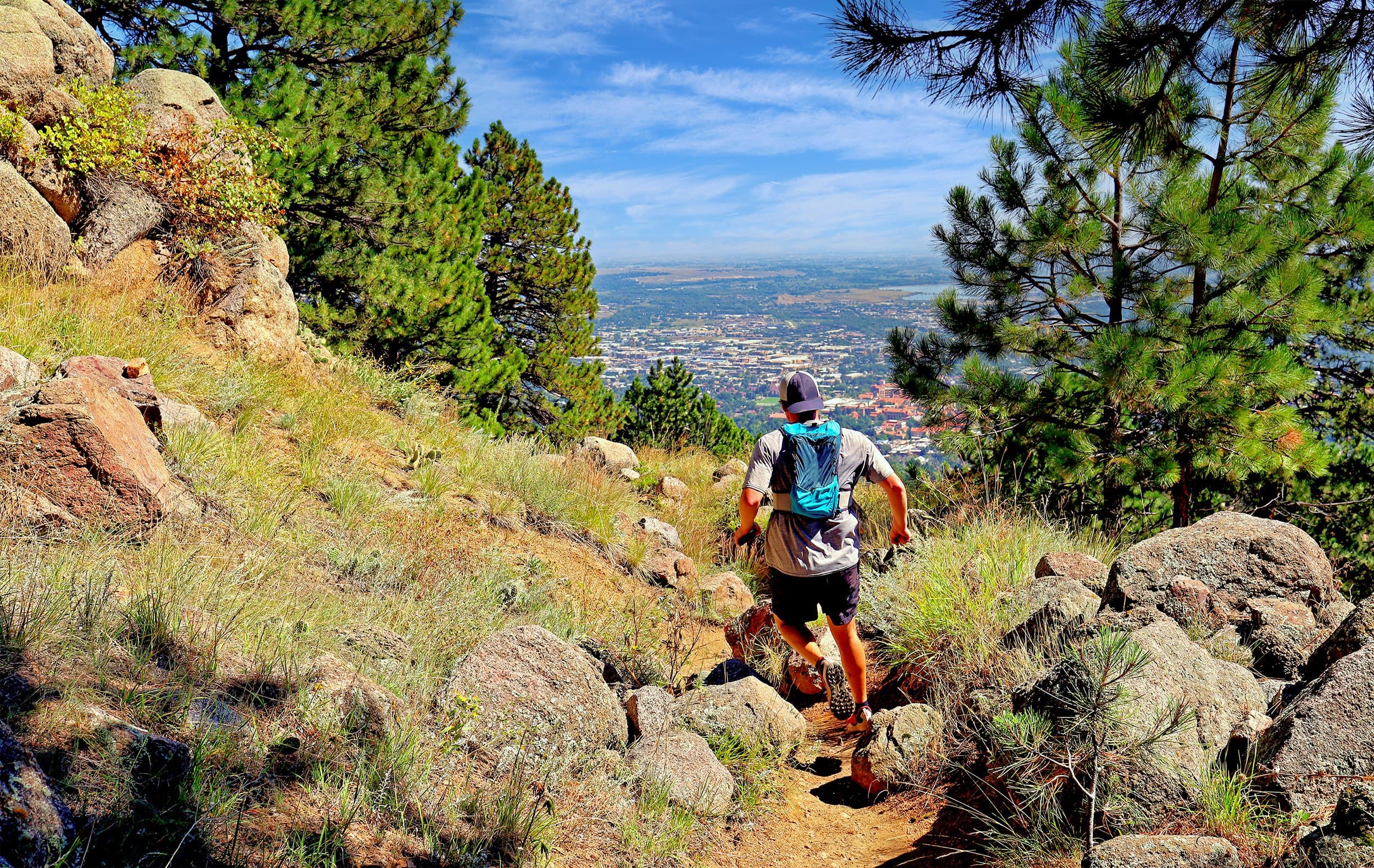 Trail runner on a winding path below Boulder's Flatirons under a clear Colorado sky