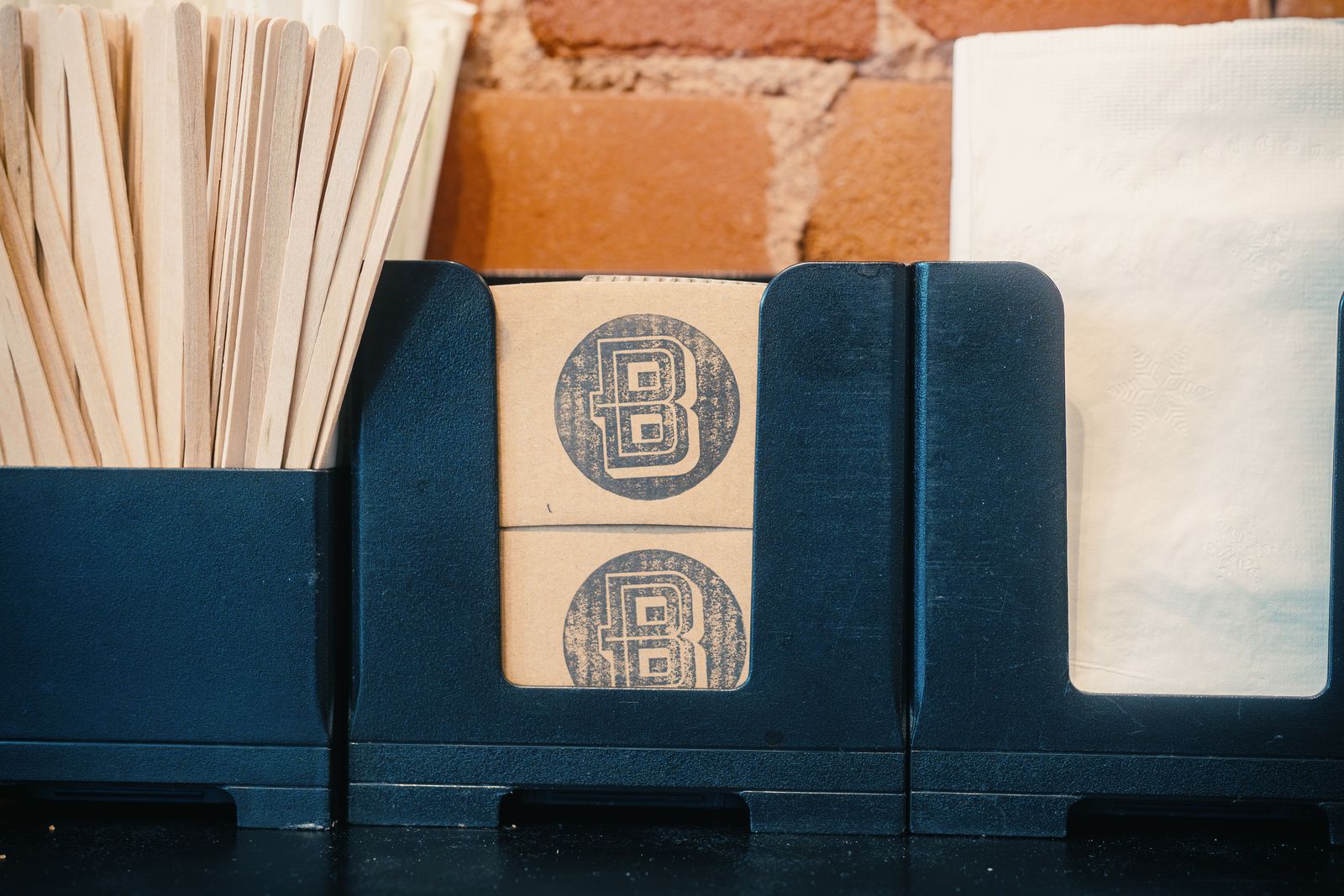 Boxcar cup sleeves stamped with the B logo, between wooden stir sticks and napkins