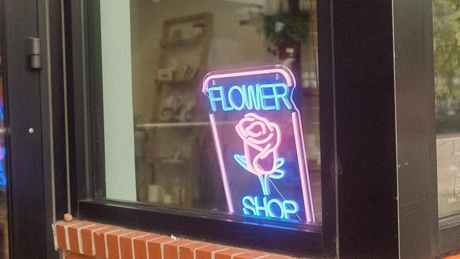 A pink and blue neon Flower Shop sign with a rose, glowing in the window at Fiori Flowers in Boulder