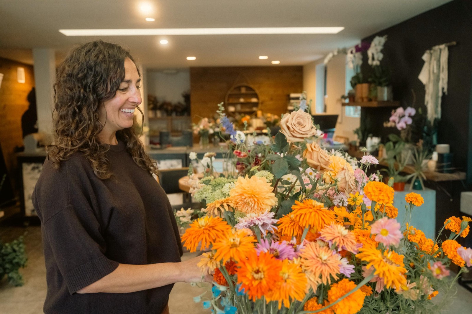 Lara of Fiori Flowers smiling as she works on a large arrangement of orange dahlias and peach roses inside her Boulder shop