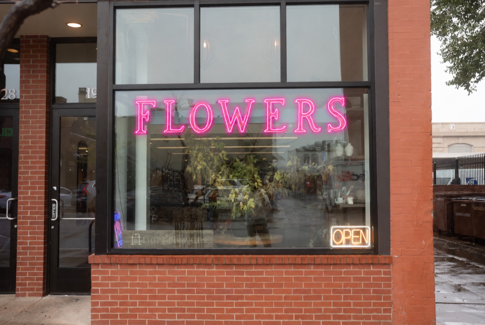 The brick storefront of Fiori Flowers on the east end of Pearl Street in Boulder, with a pink neon Flowers sign and an Open sign in the window