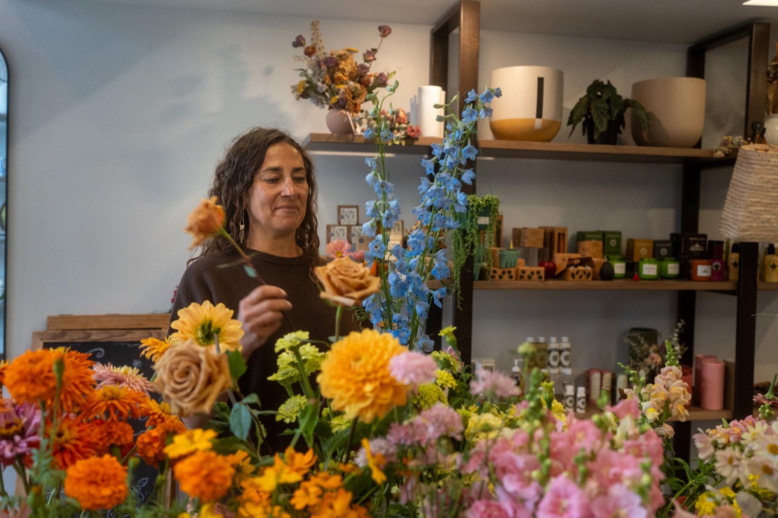 Lara arranging tall blue delphinium among orange marigolds, dahlias, peach roses and pink snapdragons at Fiori Flowers