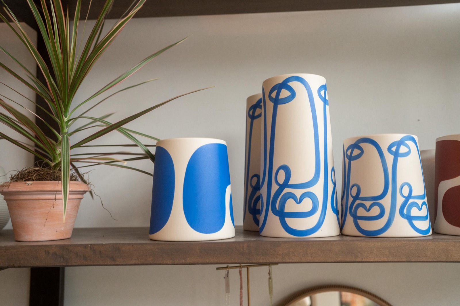 Hand-painted ceramic vases with bold blue line designs on a shelf at Fiori Flowers, beside a potted dracaena